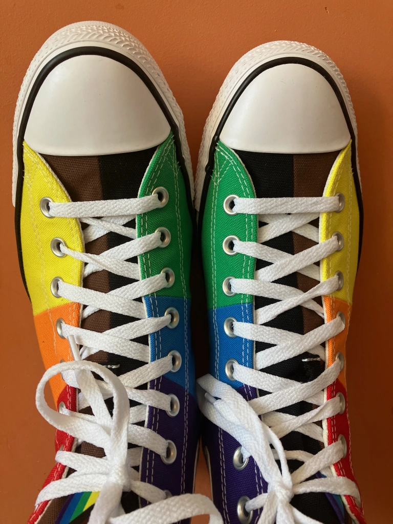A pair of trainers with rainbow stripes on them resembling the Pride flag.